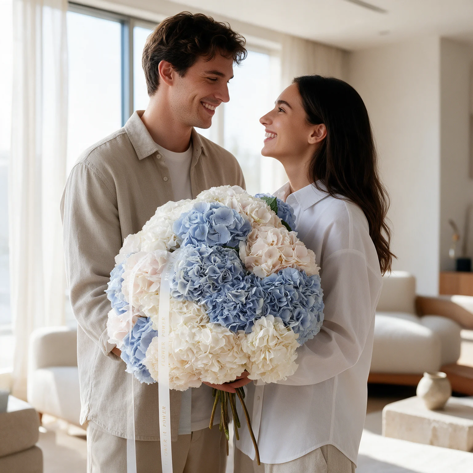 Large bouquet of blue, white and blush pink hydrangeas with green foliage, held by a couple indoors.