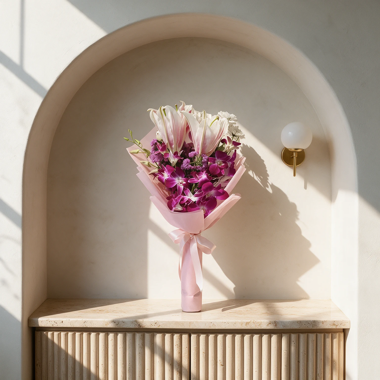 Pink lily and vivid purple orchids with green foliage, wrapped in blush pink paper and finished with a matching ribbon.