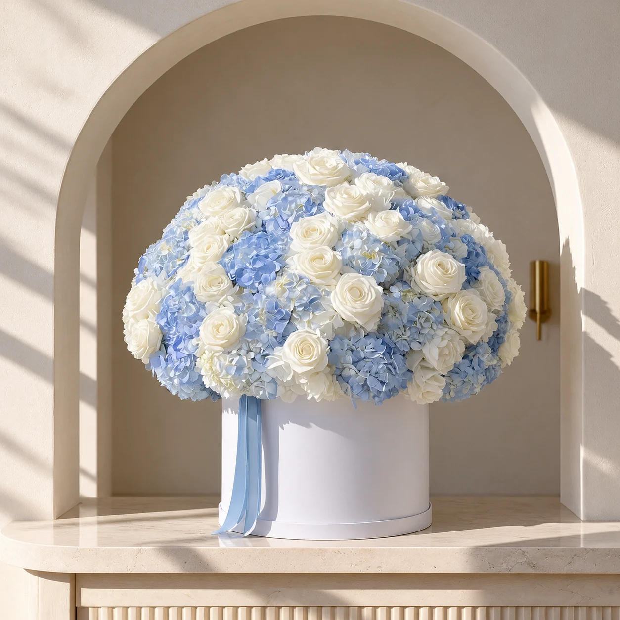 Blue hydrangeas and white roses arranged in a white cylindrical flower box with a pale blue ribbon.