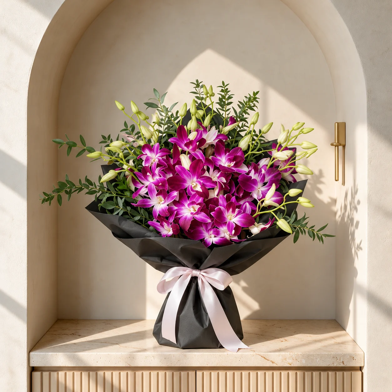 Vibrant magenta orchids with white centres and lush green foliage, wrapped in black paper with a blush pink ribbon.