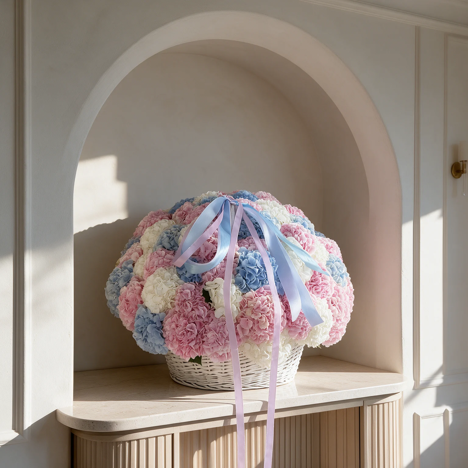 Pastel hydrangea basket featuring pink, powder blue and white flowers in a white wicker basket with pink and blue ribbons.