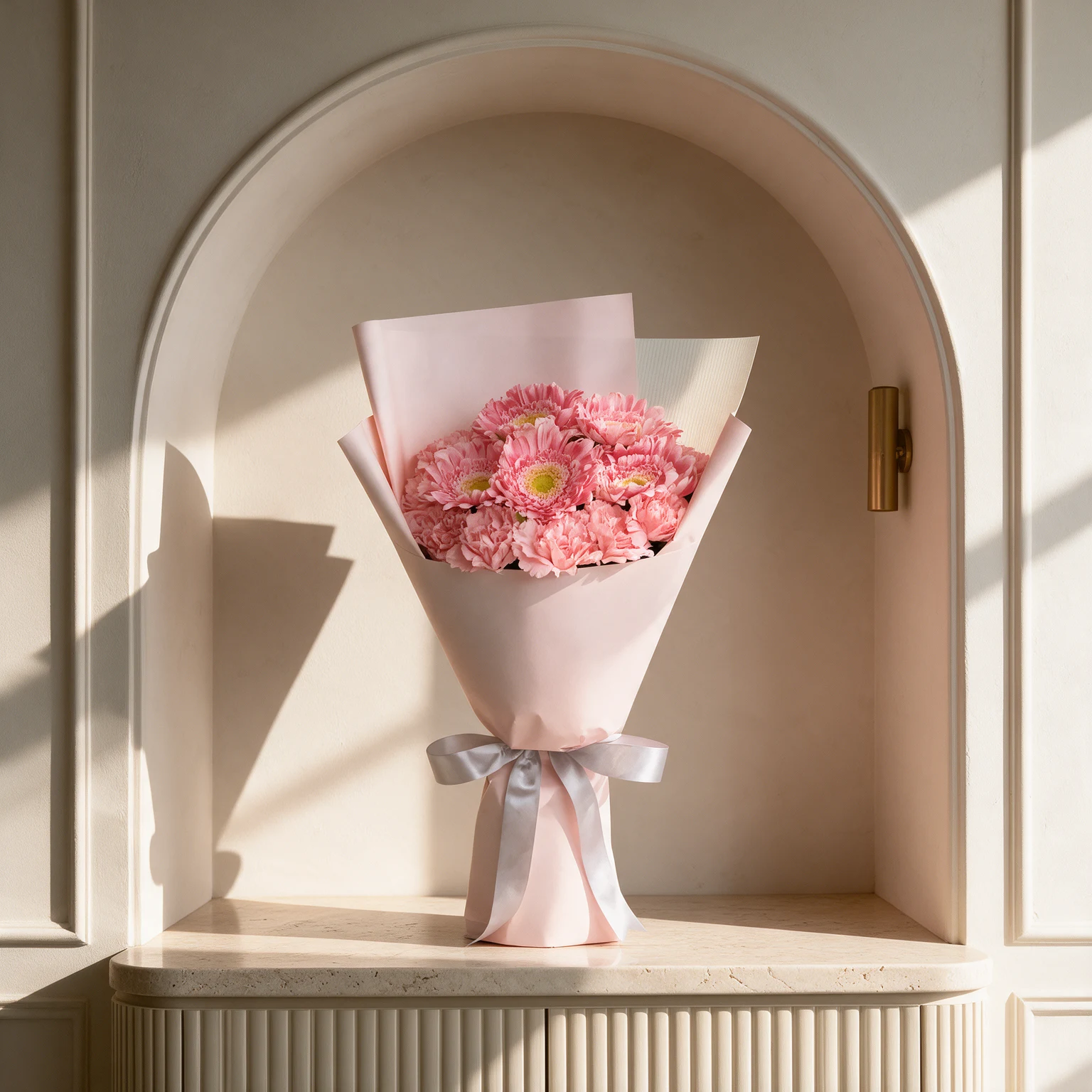 Pink gerbera daisies and complementary pink blooms arranged in blush pink wrapping with a silver satin ribbon.