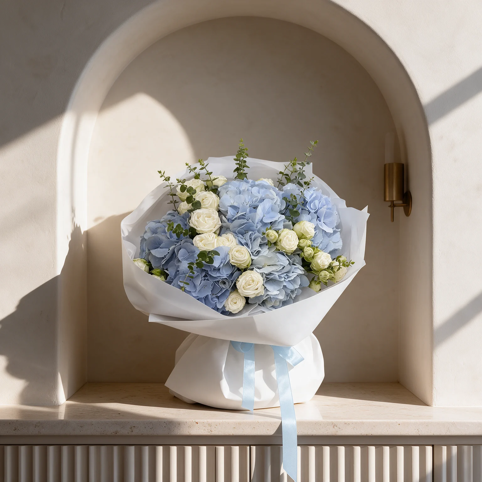 Blue hydrangeas and white roses with eucalyptus foliage, wrapped in white paper with a pale blue ribbon.