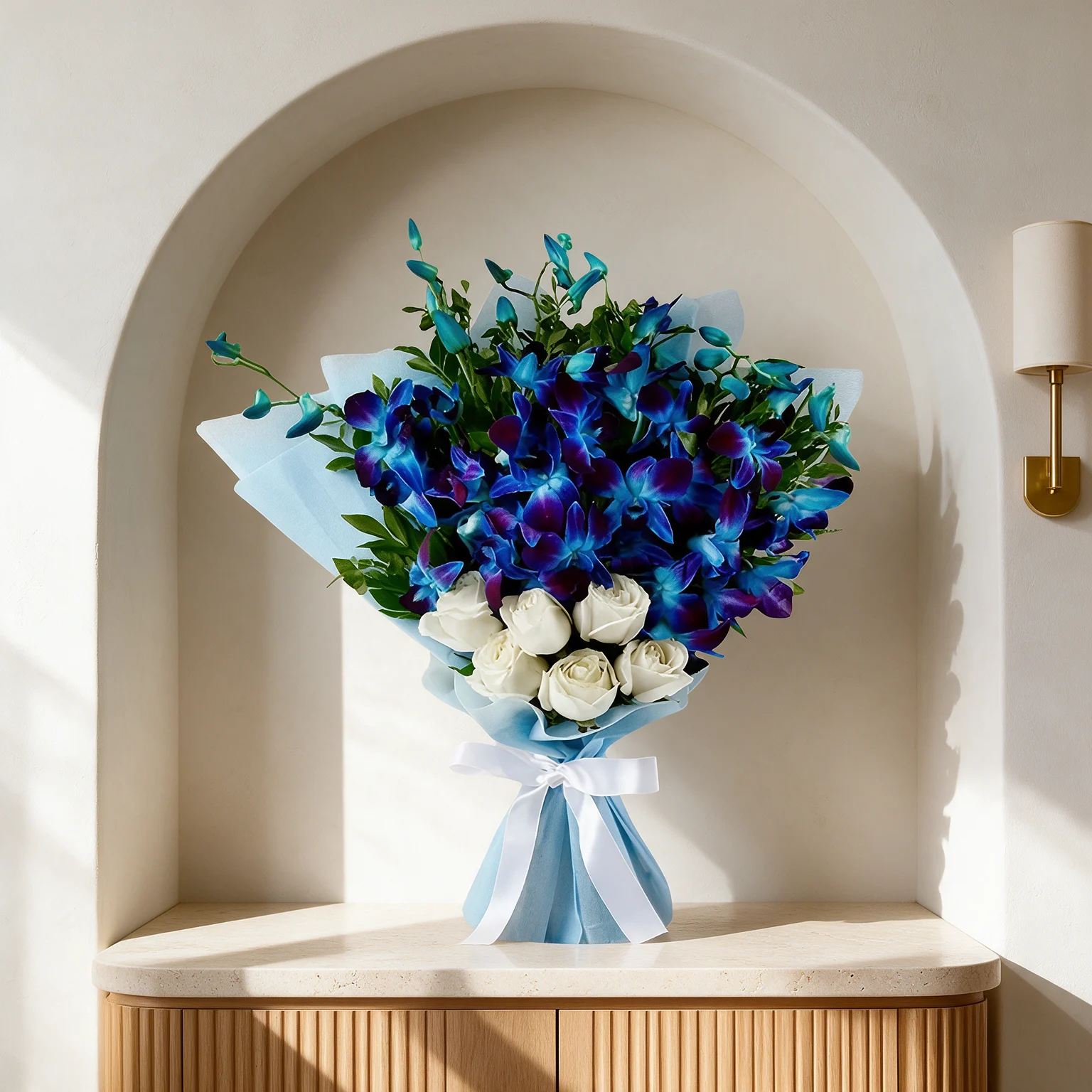 Deep blue and violet orchids with white roses and green foliage, wrapped in pale blue paper and finished with a white ribbon.