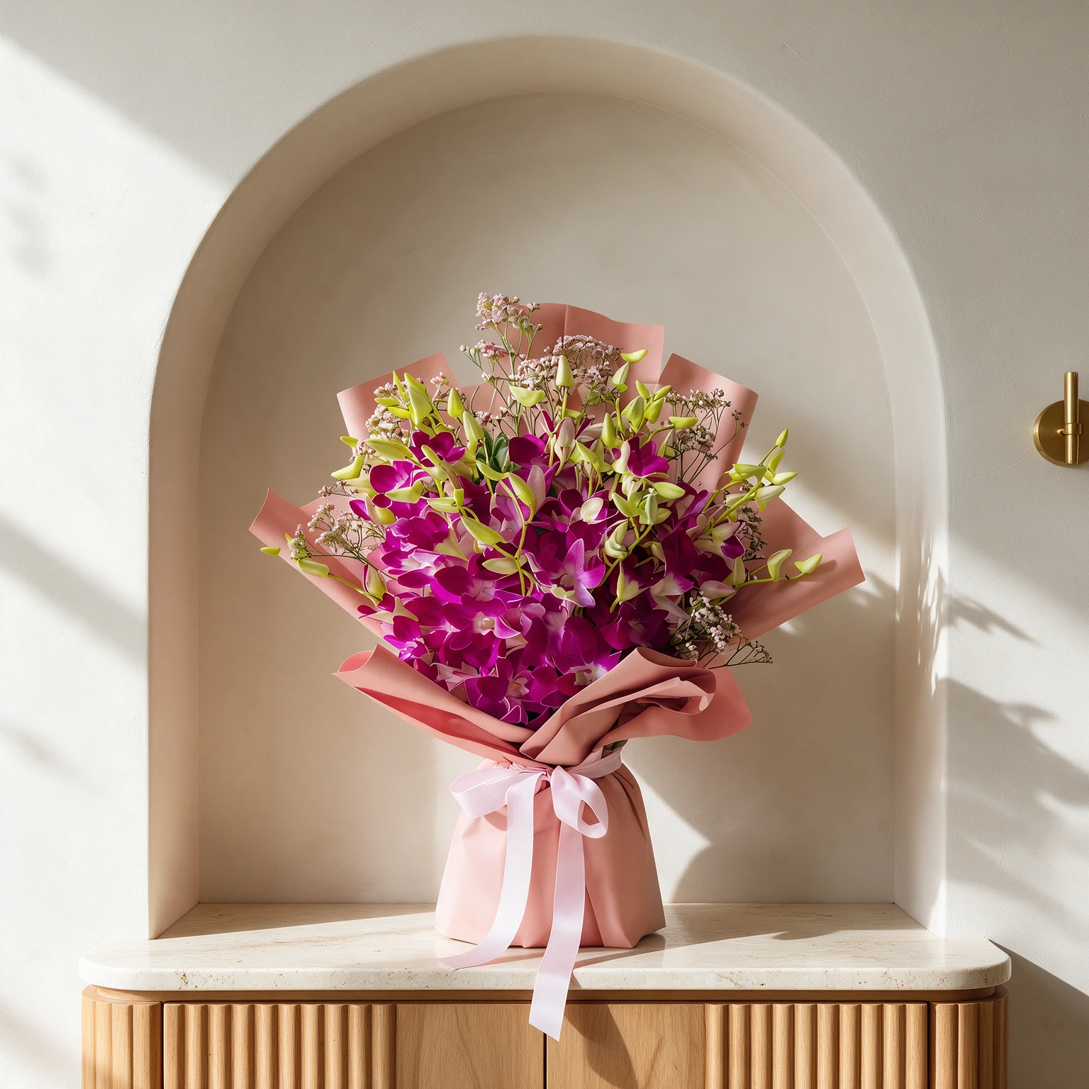 Vibrant magenta orchids with white centres and green foliage, arranged in blush pink wrapping with a pale pink ribbon.