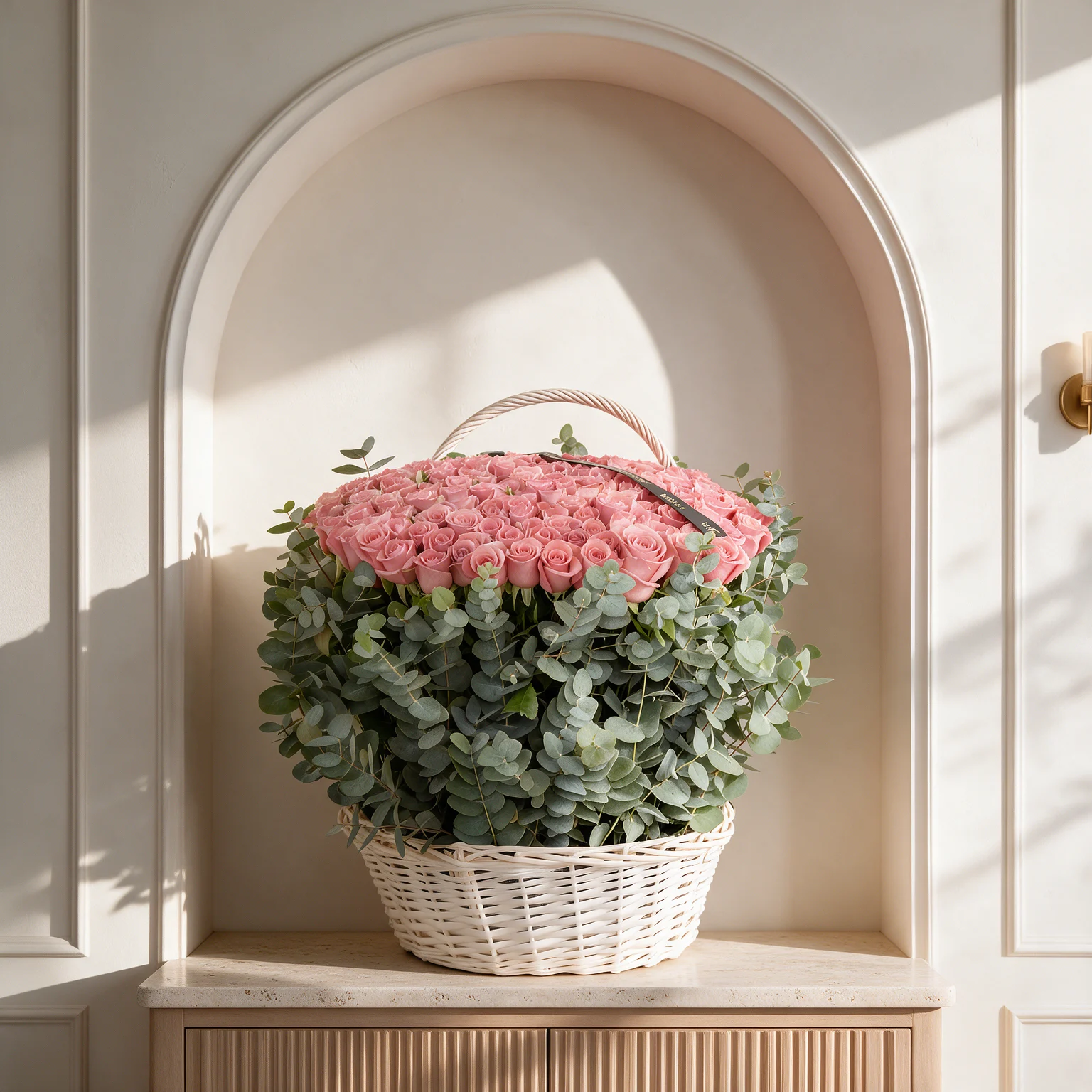 Luxury basket arrangement of 100 fresh pink roses surrounded by eucalyptus foliage for an elegant floral presentation.