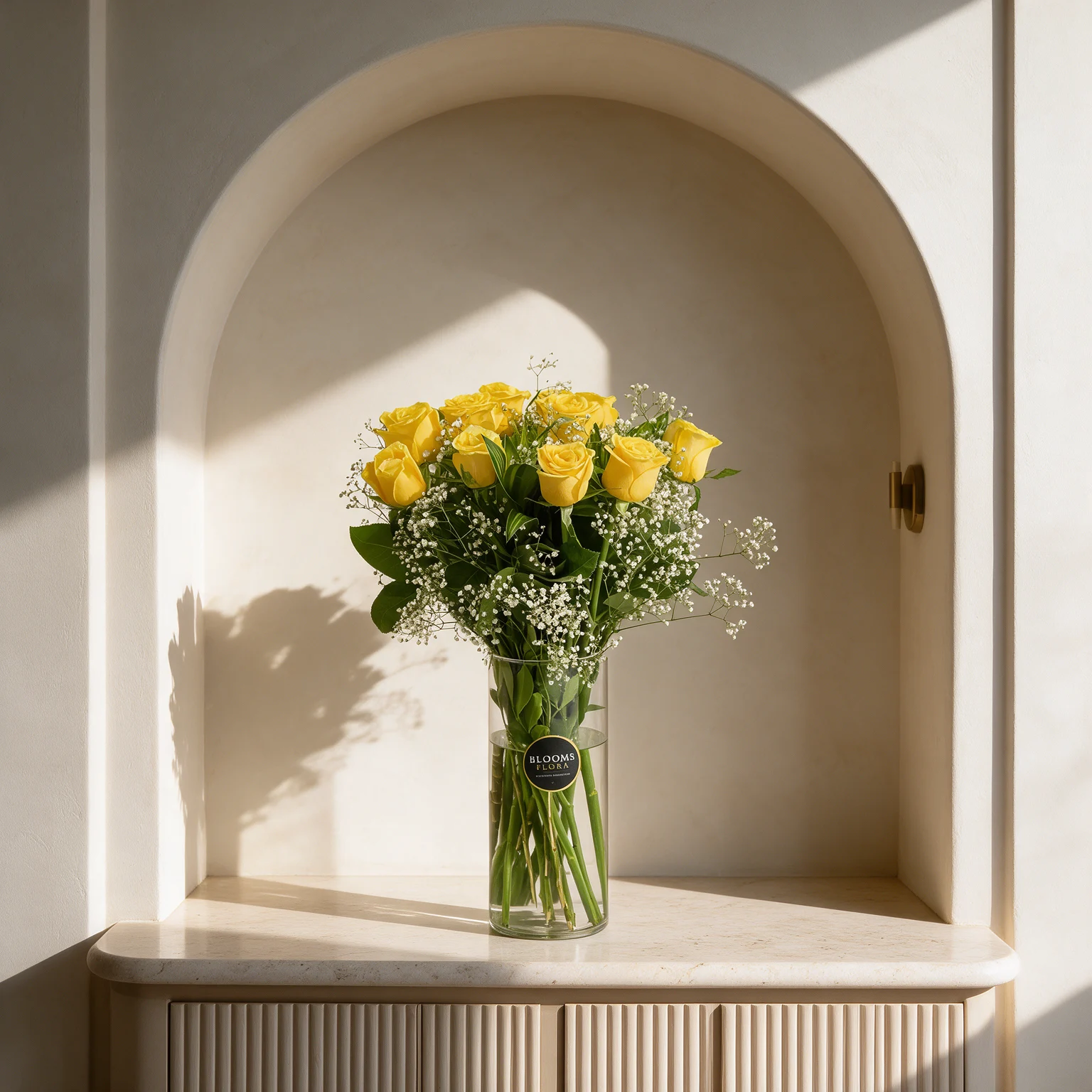10 yellow roses arranged in a glass vase with white fillers